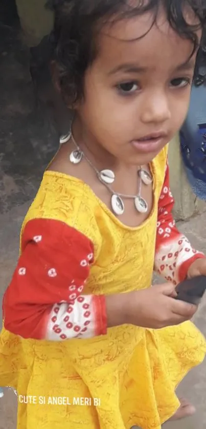 Child in a bright yellow dress, holding a toy, smiles softly.