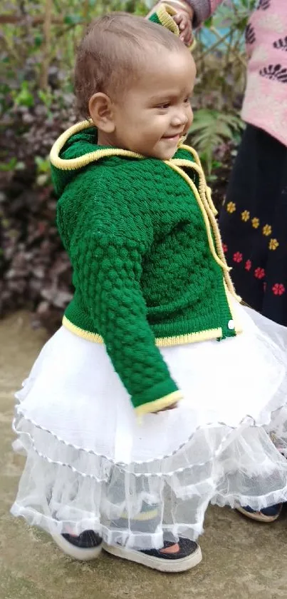 Toddler in green sweater with caregiver outdoors.