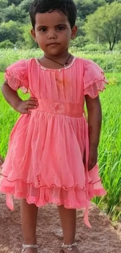 Young girl in pink dress standing in lush green field.