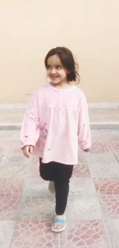 A smiling child in a pink outfit walking outdoors.