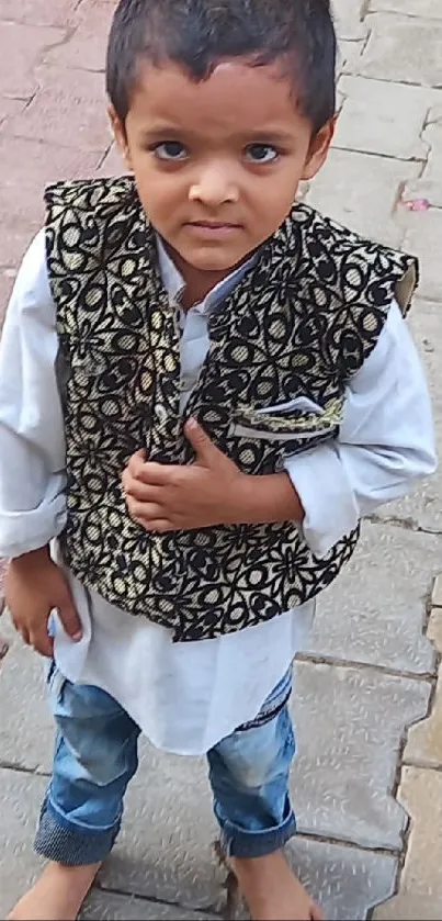 Young child in a stylish vest on a stone path.