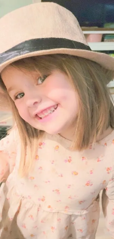 Smiling child in a beige hat and floral dress indoors.