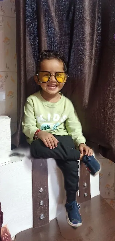 Smiling child with sunglasses in a cozy setting.