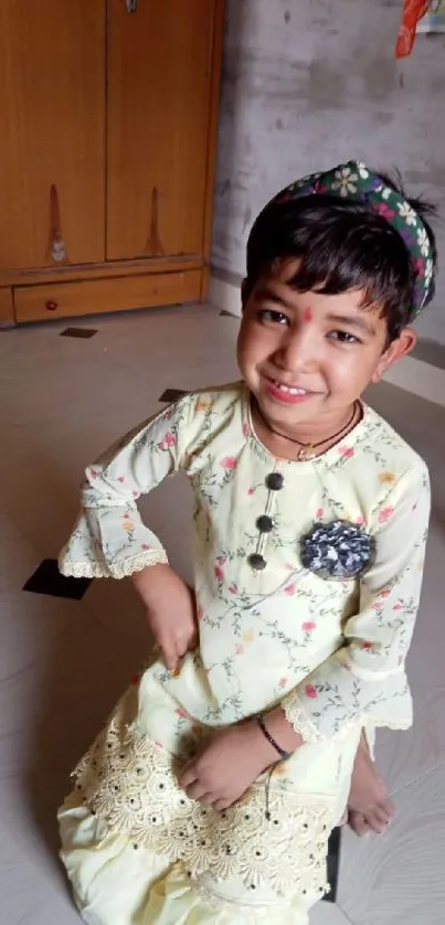 Child wearing pale yellow traditional dress, smiling indoors.