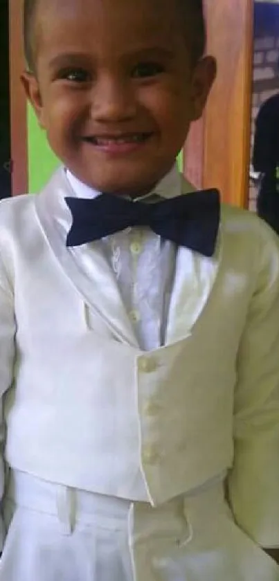 Smiling child in white suit with black bowtie, playful and joyful.