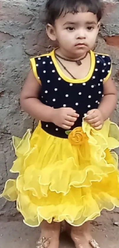 Charming child in yellow dress by a brick wall.