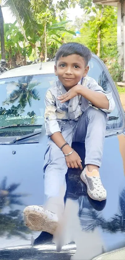 Child sitting on car, surrounded by green foliage.