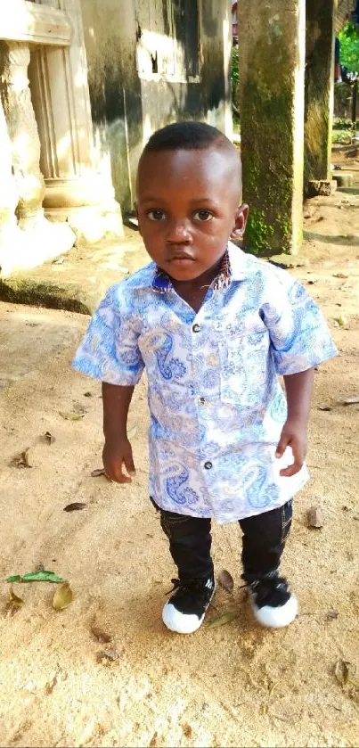 Child wearing a blue patterned shirt outdoors on a sunny day.