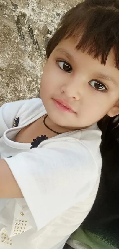 Portrait of a young child with a serene smile, against a rustic background.