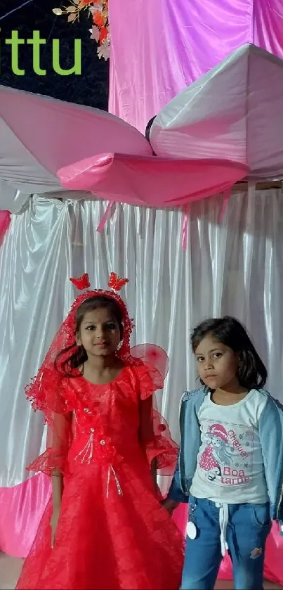 Two children in a festive red carnival setting with vibrant pink decor.