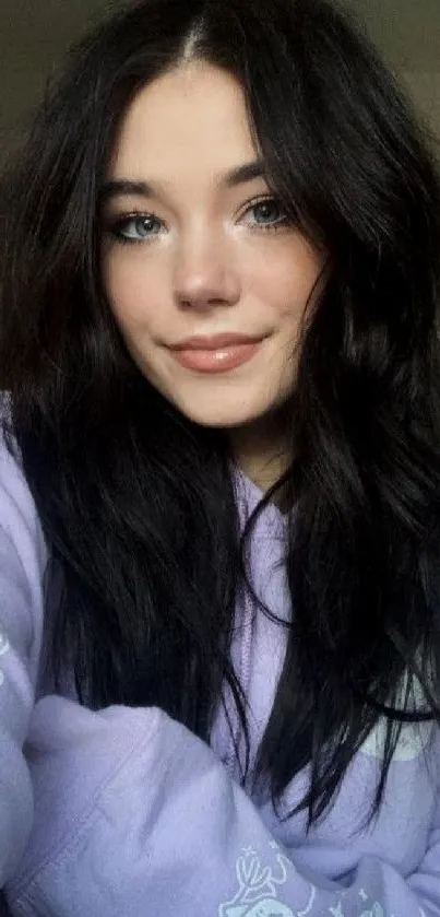 Girl in lilac hoodie with dark hair sitting indoors.