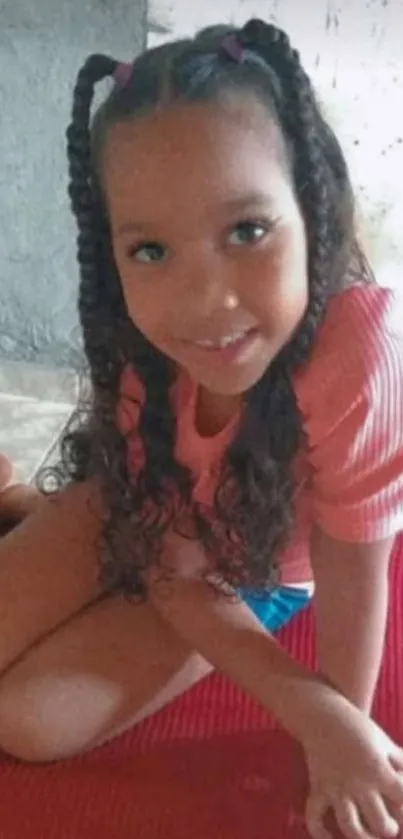 Young girl with curly hair on a red mat smiling.