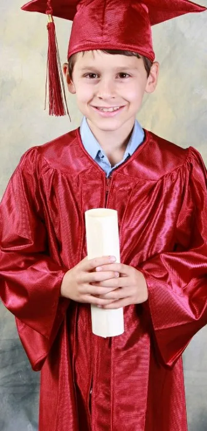 Smiling child in red graduation gown holding diploma.