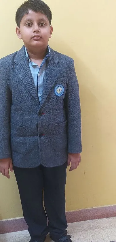 Young student in grey school uniform, standing against a beige wall.