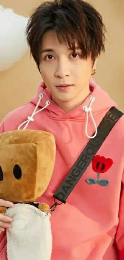 Young person in pink hoodie with plush toy against cloudy background.