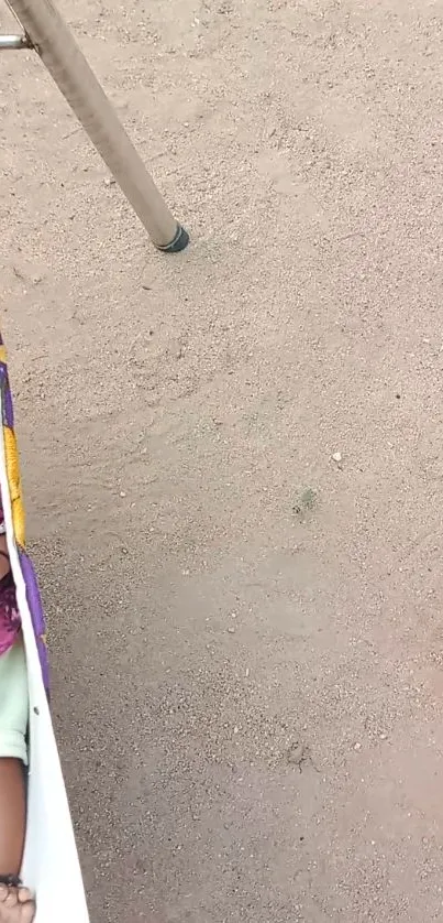 Infant peacefully sleeping in an outdoor hammock on sandy ground.