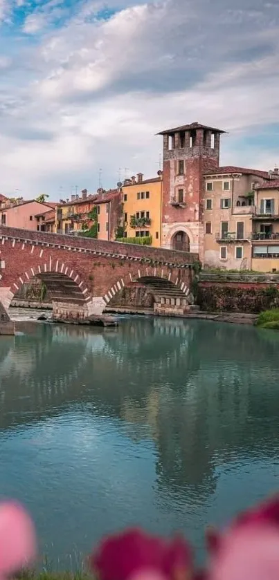 Rustic brick bridge over tranquil river with colorful buildings and sky.