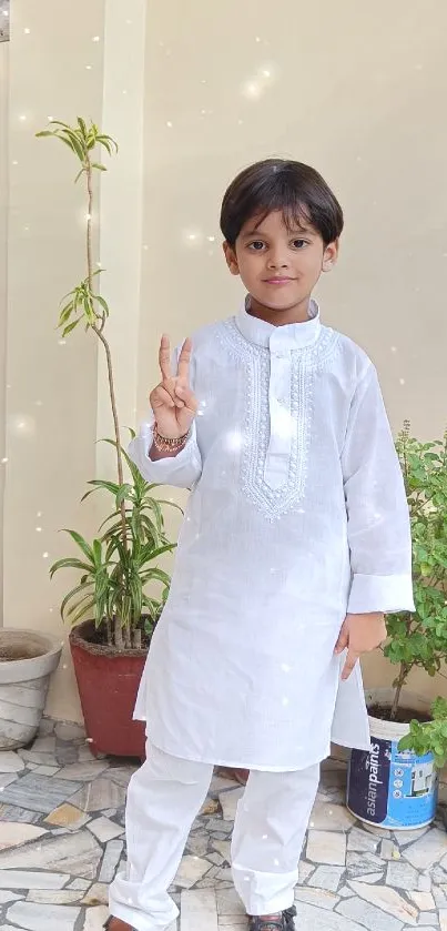 Boy in white traditional outfit with peace sign on a patio.