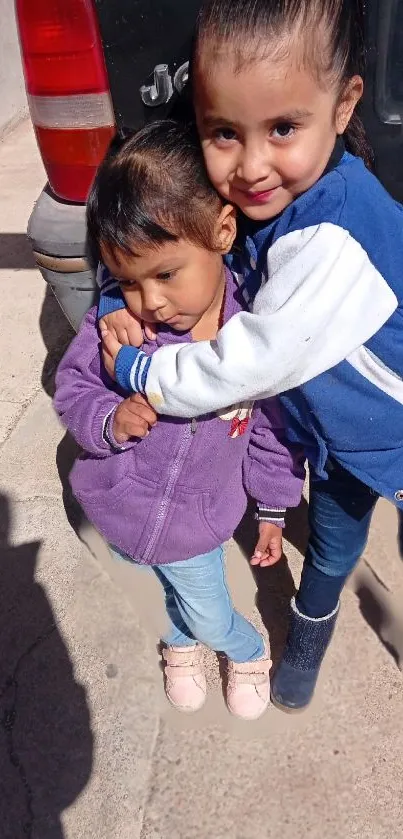 Two kids sharing a warm embrace, smiling outdoors.