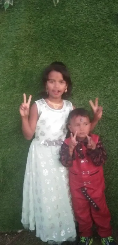 Two children pose peacefully on lush green grass, showing peace signs.