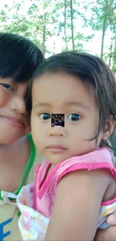 Two smiling children outdoors with green background.