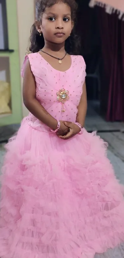 Little girl in a pink ruffled dress standing indoors.