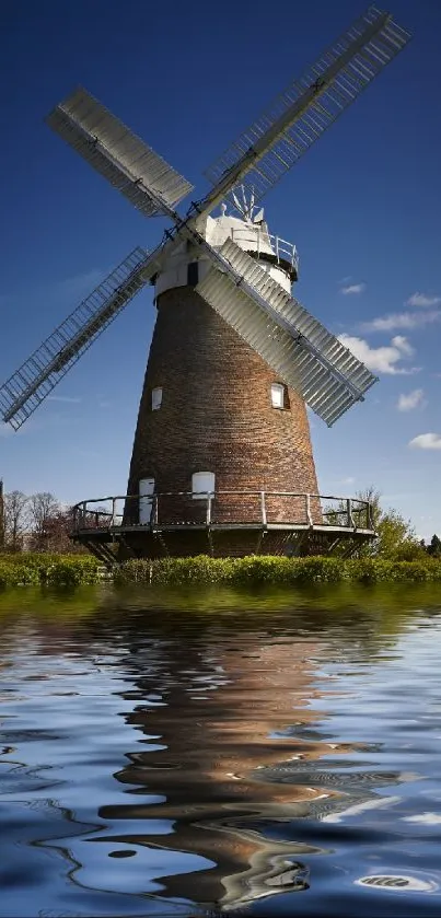 Windmill reflecting in calm water under a clear blue sky.