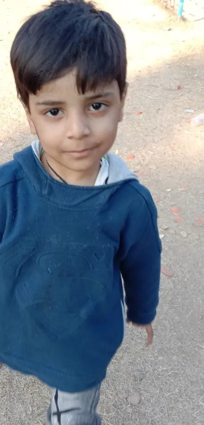 Young boy in blue sweatshirt walking outdoors on a sunny day.