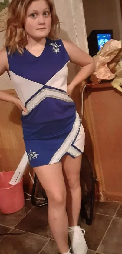 Cheerleader in blue uniform posing in a room.