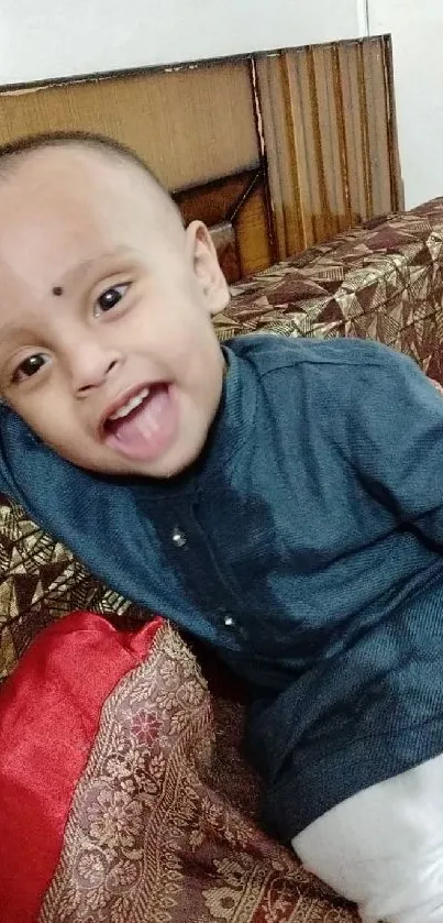 Joyful baby in blue attire on a patterned sofa, radiating happiness.