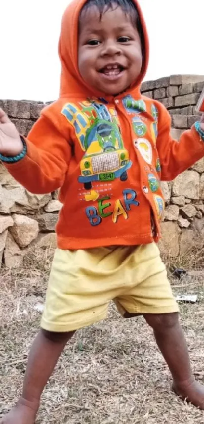 Cheerful child in orange hoodie, smiling outdoors.