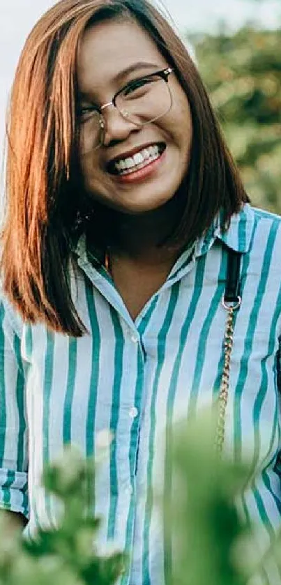 A woman smiling outdoors with a green nature background.