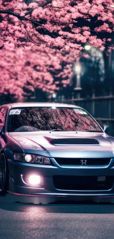 Sleek car under cherry blossoms at night.