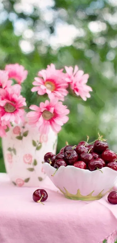 Pink flowers and cherries in bowl on tablecloth.