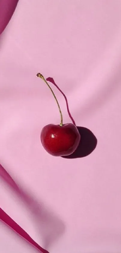 A single cherry rests on pink silk fabric with soft folds.