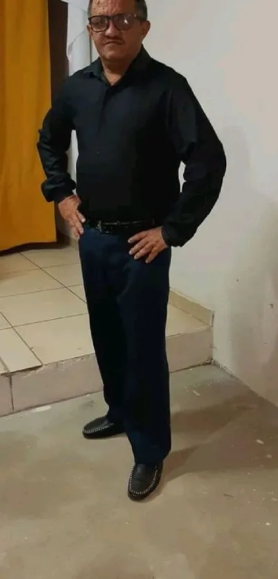 Man in a stylish black outfit striking a confident pose indoors.