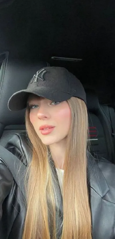 Woman in black cap and jacket inside car, taking a selfie.