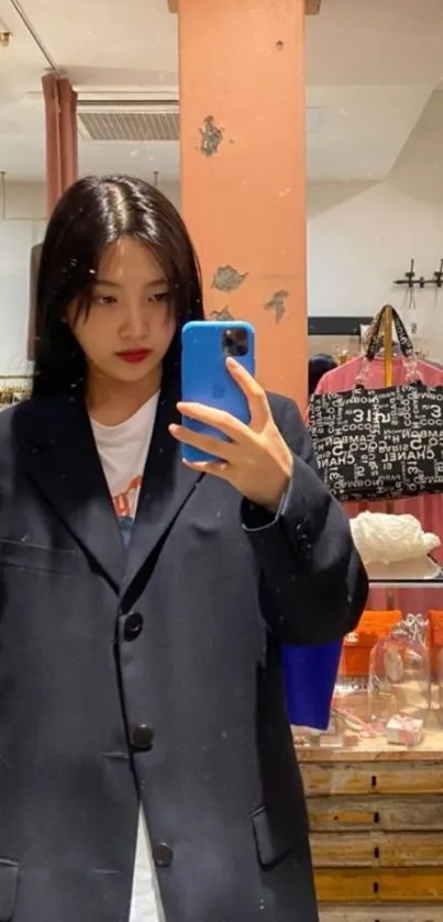 Fashionable individual takes a stylish mirror selfie wearing a black coat.