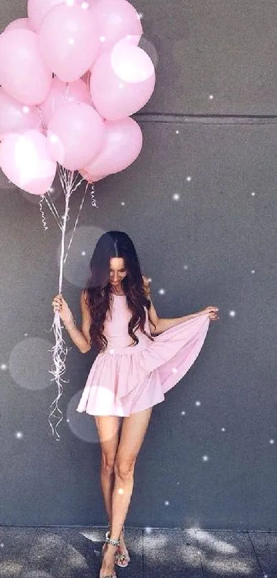 Girl in a pink dress holding balloons against a gray wall.