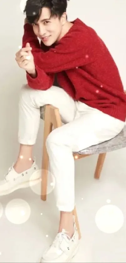 Man in a red sweater and white pants sitting on a wooden chair.