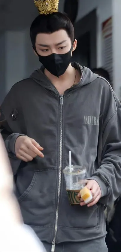 Person in gray hoodie with drink, wearing a mask.