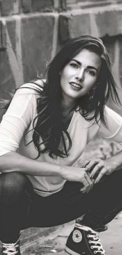 Black and white urban portrait of a young woman in casual attire crouching elegantly.