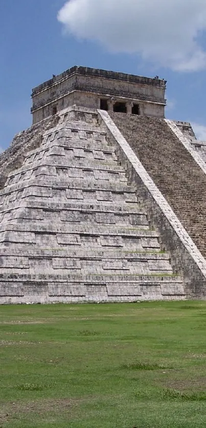 Majestic Chichen Itza pyramid under a bright blue sky with clouds and green lawn.