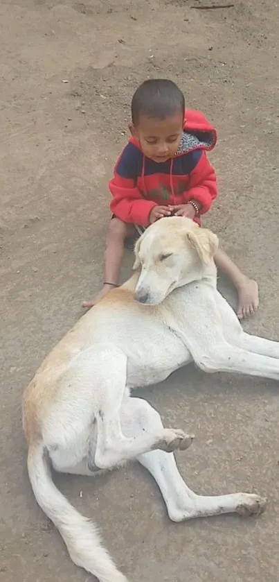 Child in red hoodie with dog lying on ground.