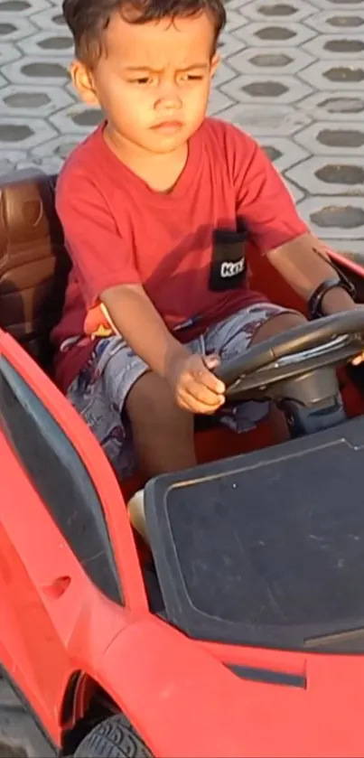 Child driving a red toy car on a sunny day.