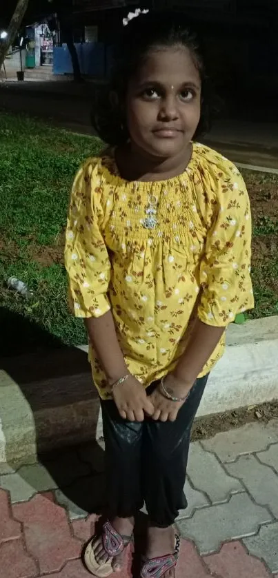 Girl in a yellow floral dress standing outdoors at night.