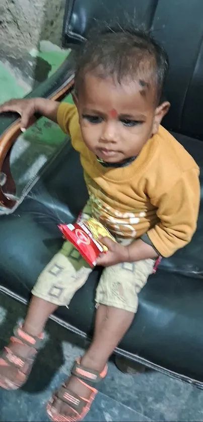 Child on black leather chair holding a snack.