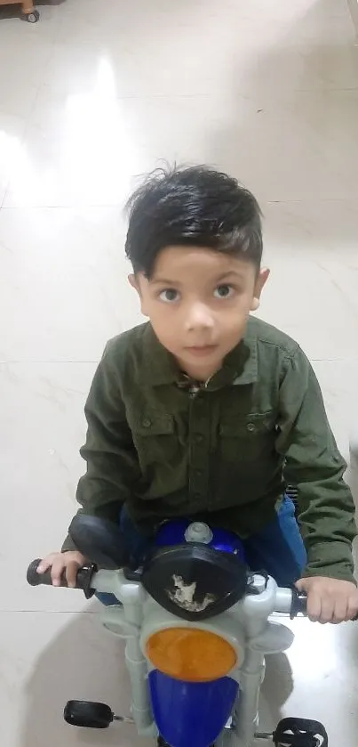 Child on a blue toy motorcycle with green shirt indoors.