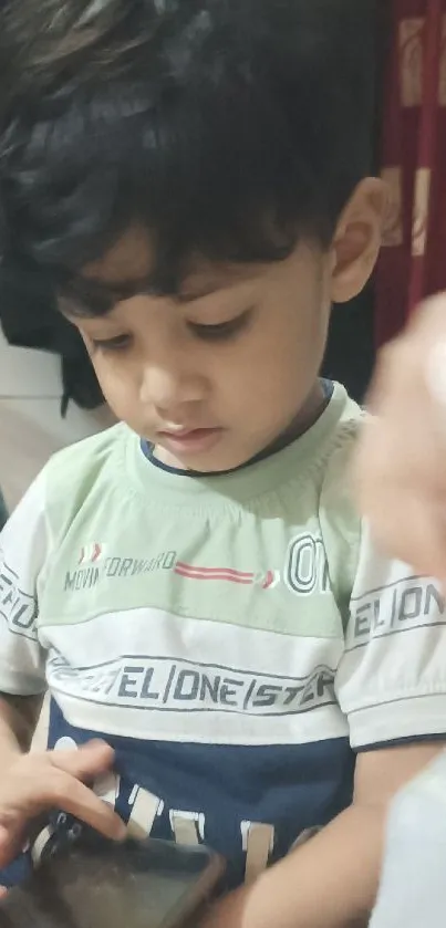 A child in a green shirt using a smartphone indoors.