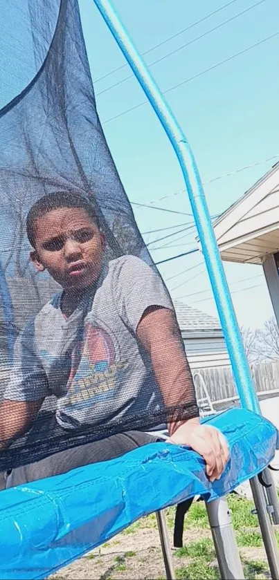 Child sitting on a trampoline under a clear sky.